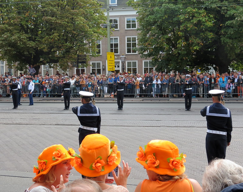 Prinsjesdag in Den Haag. Drie vrouwen met oranje hoeden kijken naar de weg waar de optocht langs zal rijden.