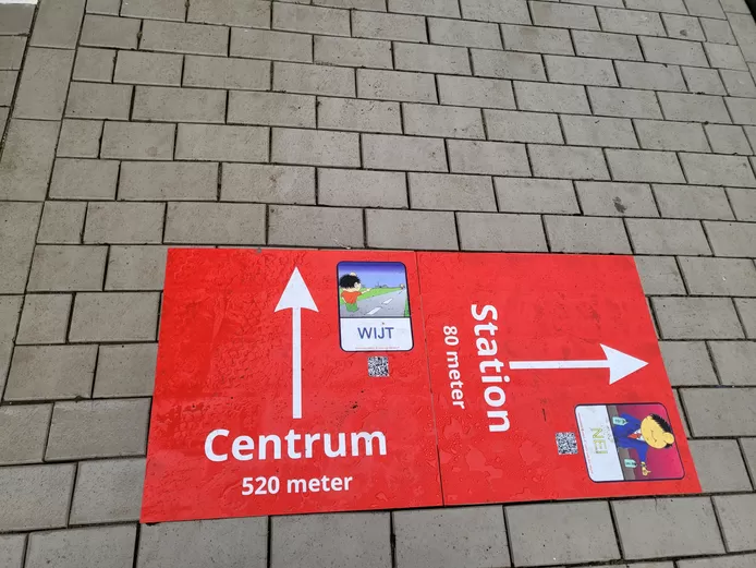 Sticker in Helmond met bewegwijzering in het rood. Het centrum is 520m rechtdoor met het Helmondse woord 'wijt', en het station is 80m naar rechts met het Helmondse woord 'nei' erbij. 