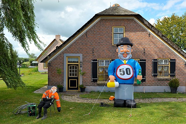 Foto van een opblaasbare Abraham pop in de voortuin van een huis. Abraham heeft een pul bier in de hand, een rond bord met het getal vijftig op zijn buik, grijze haren en baard, en een hoge hoed.