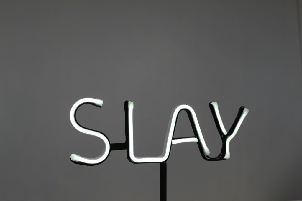 Zwart-wit foto van een grijze achtergrond met in lichtjes het woord "slay" als voorbeeld van Gen Z-taal.