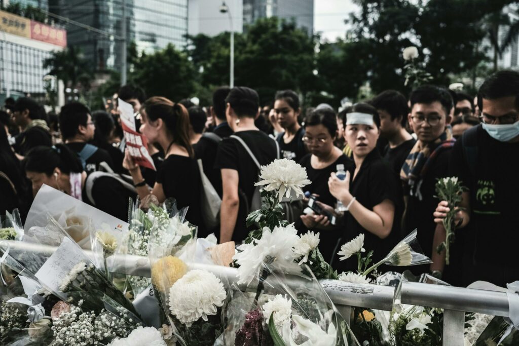 bloemen die zijn neergelegd achter dranghekken, op de achtergrond mensen die aan het rouwen zijn in het openbaar 