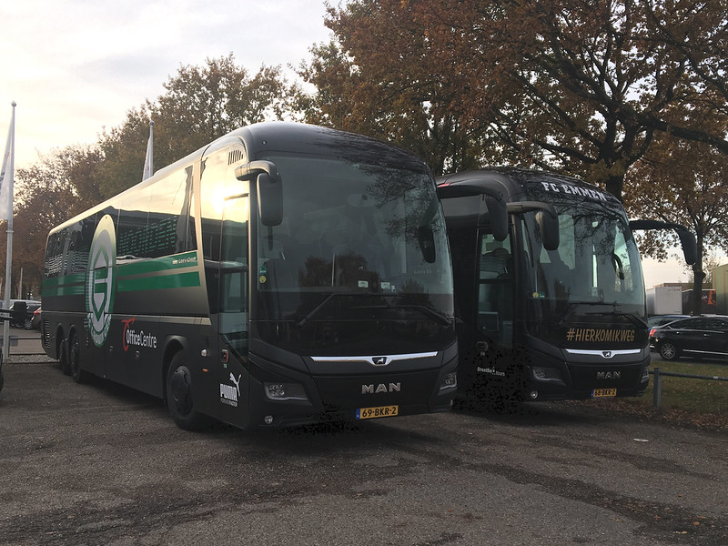 Foto van twee spelersbussen van FC Emmen met op de voorkant #Hierkomikweg.